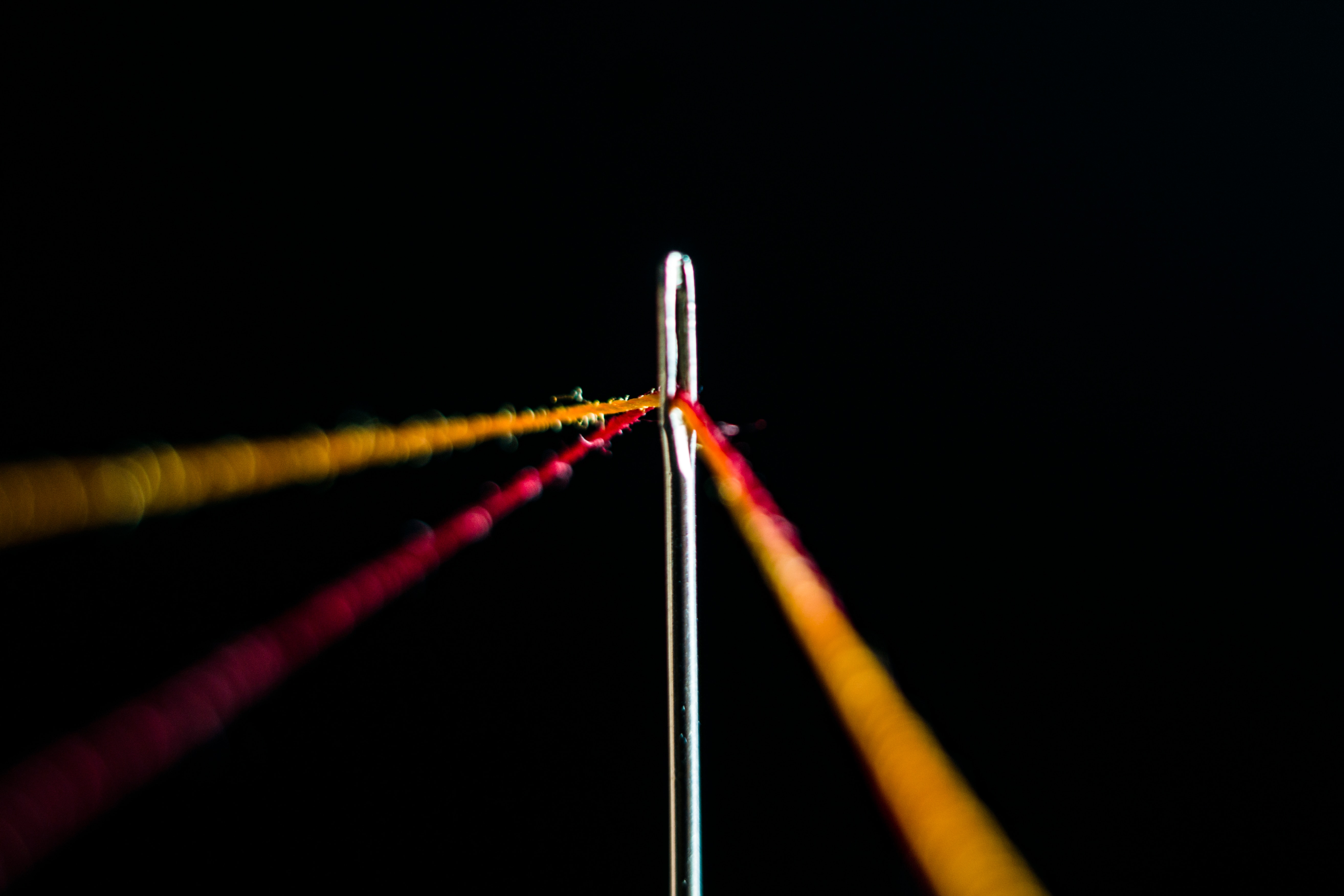 Eine Nadel mit zwei durch sie gespannten Fäden vor einem schwarzen Hintergrund