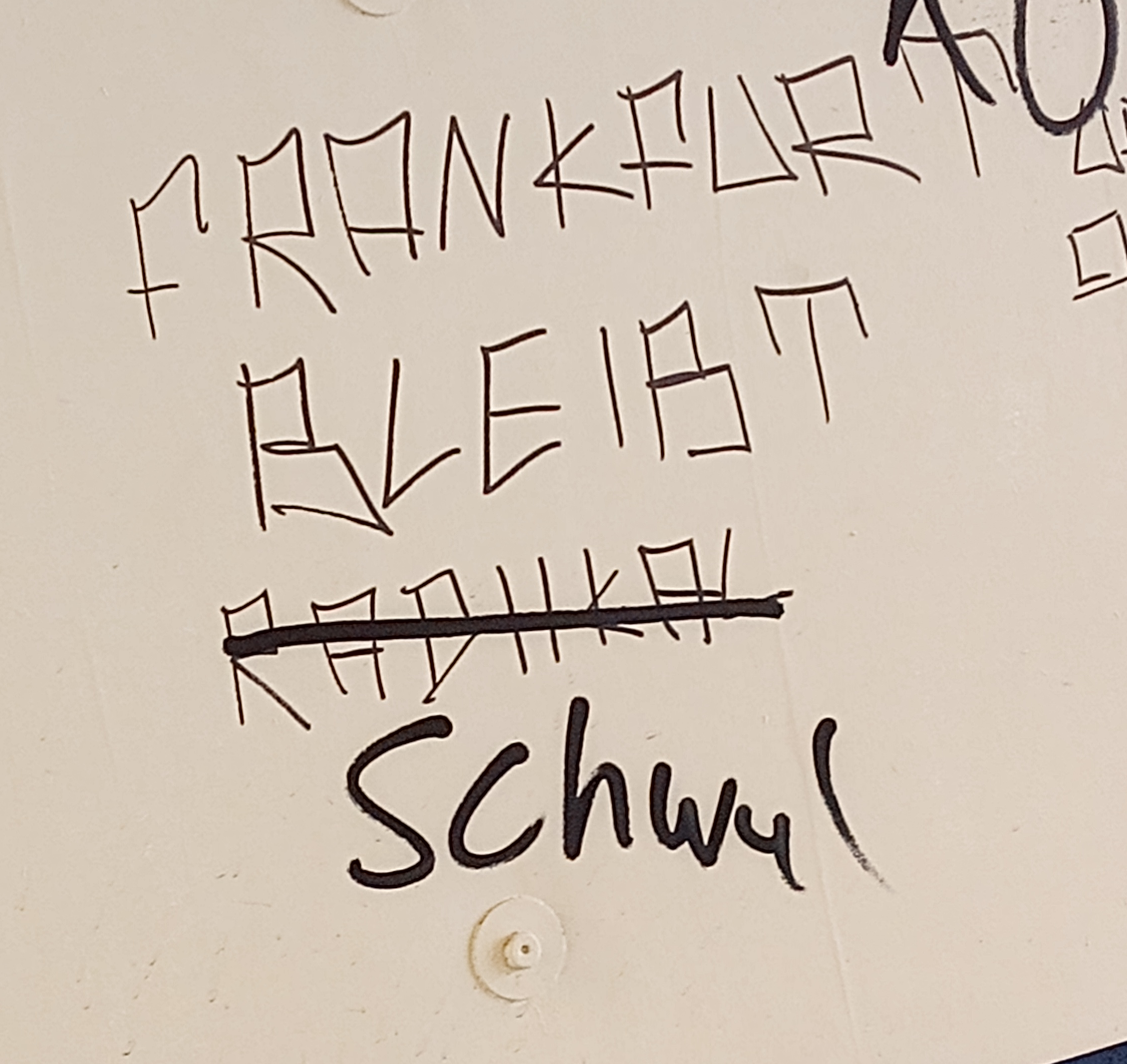 Graffiti an einer weißen Wand: 'Frankfurt bleibt radikal'. 'Radikal' ist durchgestrichen, stattdessen hat dort jemand 'schwul' hingeschrieben