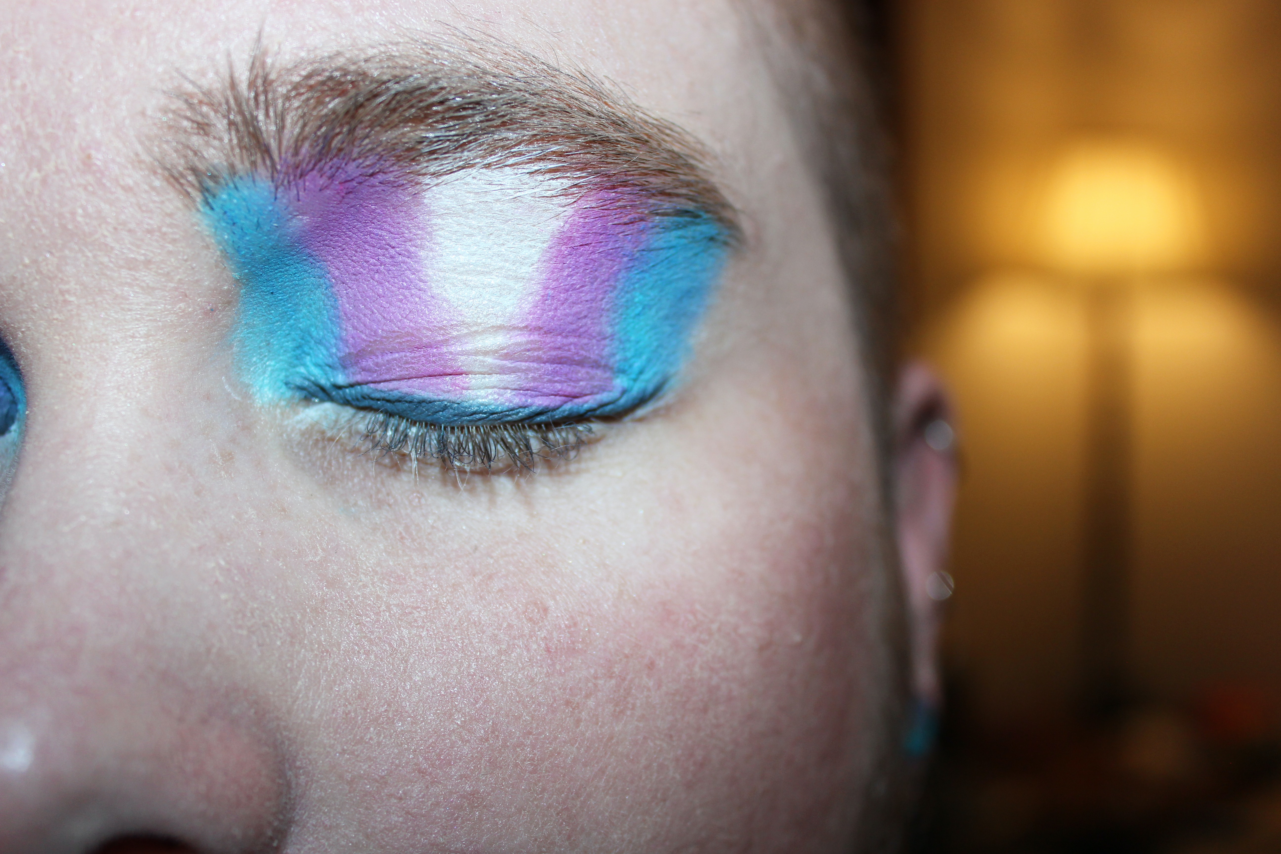 Eine Person mit geschlossenen Augen und Lidschatten in trans Pride-Farben